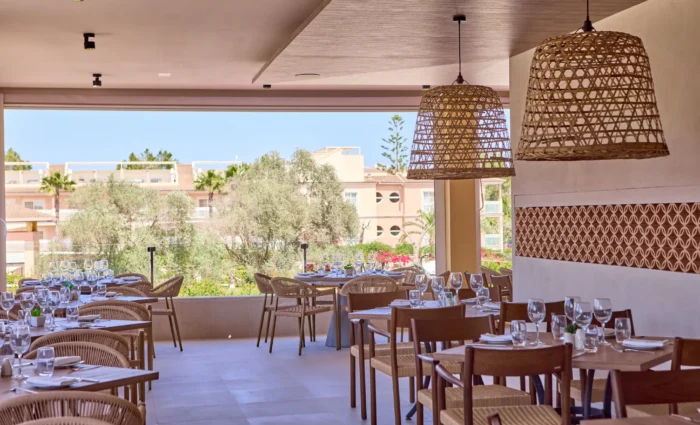 Sfeervol restaurant La Tavola van Zafiro Can Picafort met gedekte tafels, rieten hanglampen en uitzicht op de tuin.
