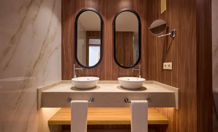 Moderne badkamer van een suite in Zafiro Can Picafort met dubbele wastafel, ovale spiegels en houtaccenten.