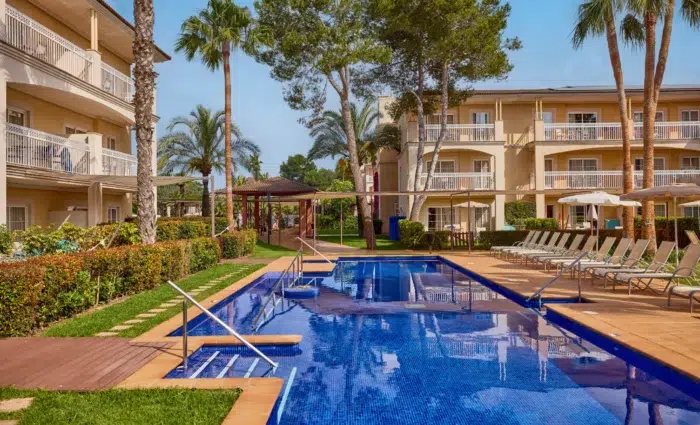 Rustig swim-up zwembad bij Zafiro Can Picafort met ligbedden, palmbomen en suites met balkon.