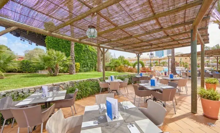 Gezellig buitenterras van Zafiro Can Picafort op Mallorca met gedekte tafels, rieten overkapping en groene tuin.